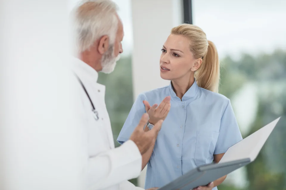 A senior doctor talking with a younger colleague who is holding a folder