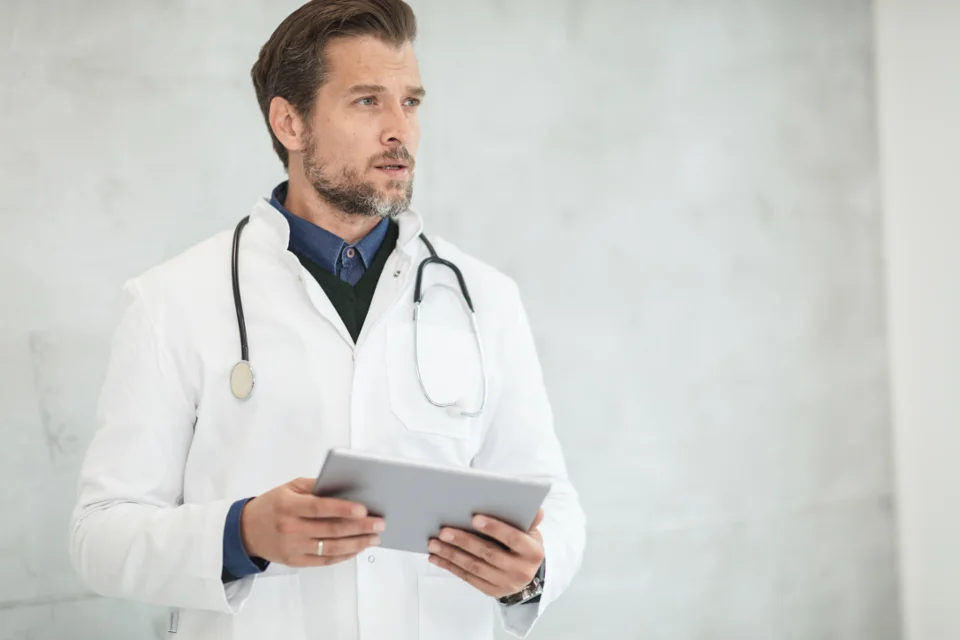 A doctor in a white coat with a stethoscope, holding a tablet