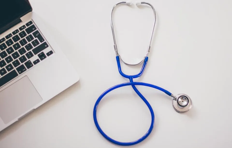 A stethoscope resting on a desk beside an open laptop