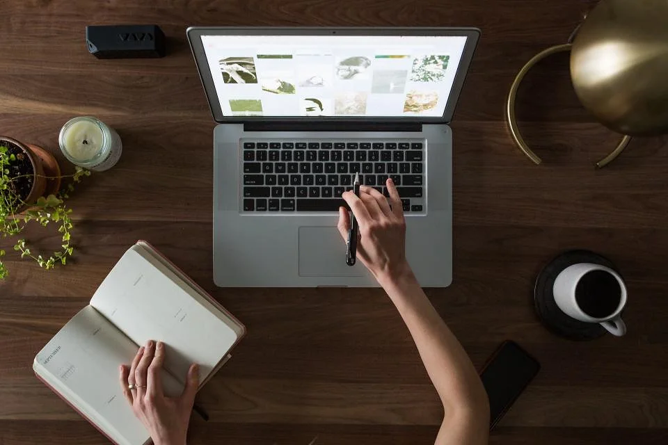 Overhead view of a desk with a laptop, an open notebook and a cup of coffee